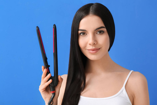 Beautiful young woman with flattening iron on color background - Photo, Image