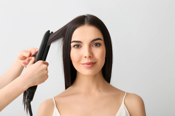 Straightening of young woman's hair on light background - Foto, Imagem