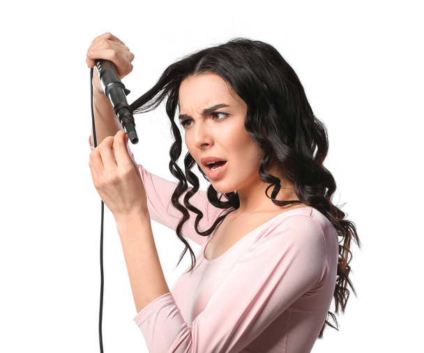Стрессовая молодая женщина с щипцами для завивки на белом фоне - Фото, изображение