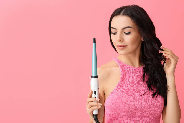 Beautiful young woman with curling iron on color background - Photo, Image