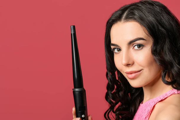 Beautiful young woman with curling iron on color background - Φωτογραφία, εικόνα