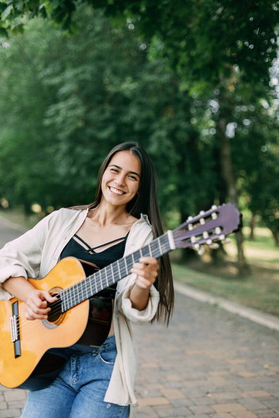A beautiful girl plays the guitar, walks along the alley in the park. Music, musician, guitar, freedom - 写真・画像