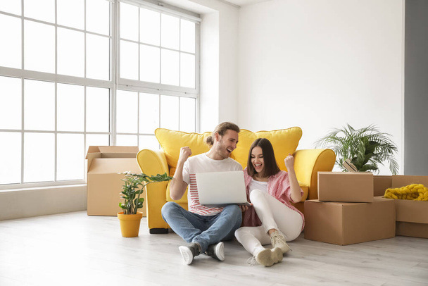 Young couple using laptop in their new house on moving day - Photo, Image