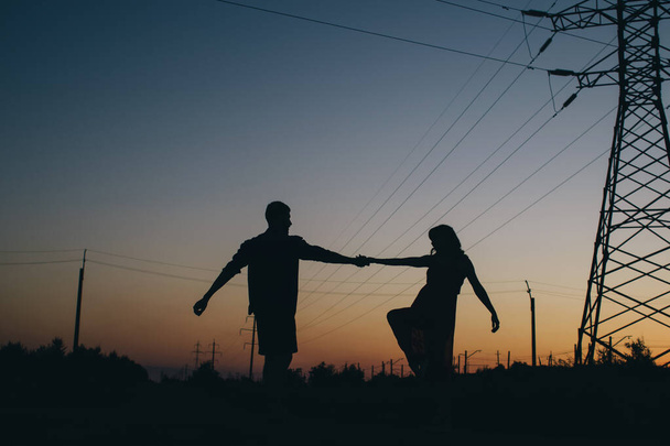 Couple dancing on the background of the sunset. Only the shadows and silhouettes of a man and a woman are visible. Dancers in the field. Next to a romantic pair of power lines. Romance and passion - Φωτογραφία, εικόνα