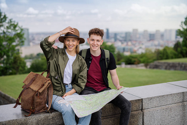 Young couple travelers with map in city on holiday, resting and looking at camera. - Foto, imagen