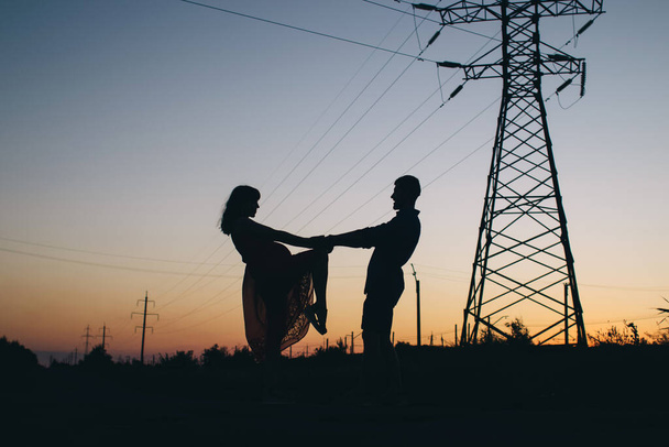 Couple dansant sur le fond du coucher du soleil. Seules les ombres et les silhouettes d'un homme et d'une femme sont visibles. Des danseurs sur le terrain. À côté d'une paire romantique de lignes électriques. Romance et passion - Photo, image