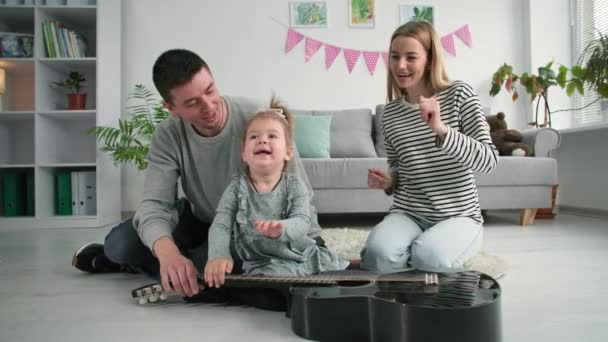 τρόπος ζωής, ευτυχισμένη οικογένεια μικρό θηλυκό παιδί παίζει μουσικό όργανο χαρούμενη χαρούμενη χαρούμενη μπαμπάς και η μαμά παλαμάκια χέρια στο σαλόνι - Πλάνα, βίντεο