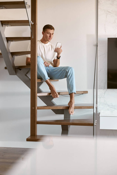 Relaxing happy caucasian man on the minimalistic stairs in modern light apartment - Foto, Imagem
