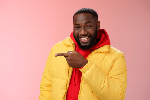 Charismatic carefree handsome black bearded guy in yellow jacket laughing friendly look camera chat pointing left show cool place hang out standing joyful pink background talking having fun - Zdjęcie, obraz