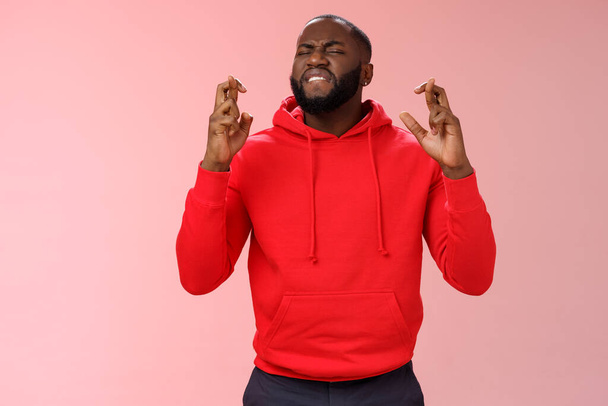 Пристрасний афро-американський шанувальник чоловічої статі молиться хрест пальці удачі, просячи Бога виграти парі кусаючи губу нетерпляче чекаючи важливих результатів, сподіваючись, що стоїть рожевий фон
 - Фото, зображення