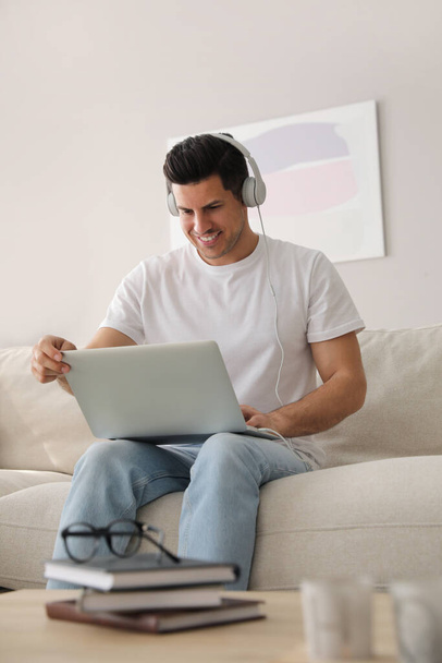 Man with laptop and headphones sitting on sofa at home - Foto, imagen