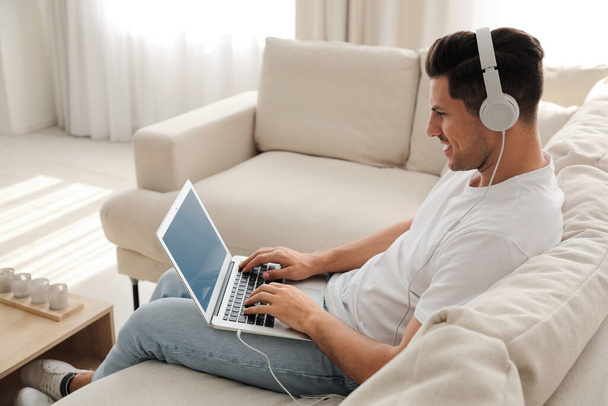 Man with laptop and headphones sitting on sofa at home - Foto, Imagen