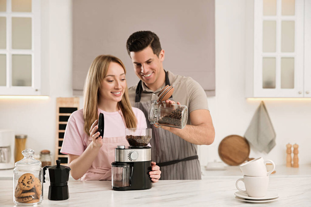 Lovely couple using electric coffee grinder together in kitchen - Valokuva, kuva
