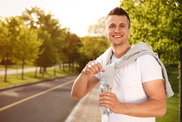 Young man with bottle of water outdoors. Morning fitness - Foto, imagen