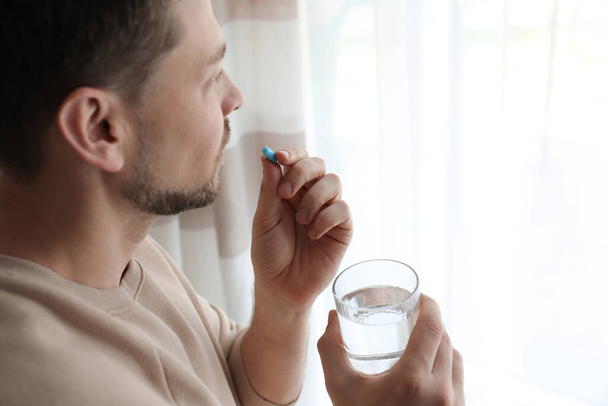 Man with glass of water taking pill at home - Valokuva, kuva