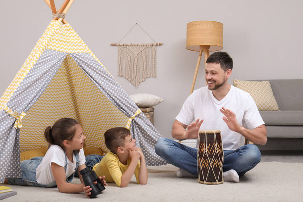 Father and children playing near toy wigwam at home - Фото, зображення