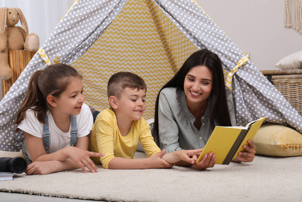 Mother with children reading book in wigwam at home - Foto, Imagen