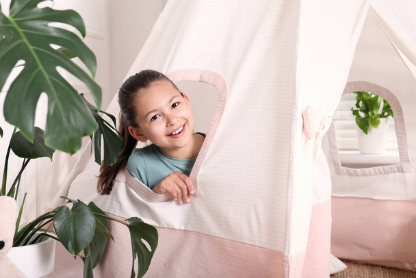 Cute little girl peeking out window of toy wigwam at home - Photo, Image