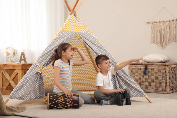 Cute little children playing in toy wigwam at home - Foto, afbeelding