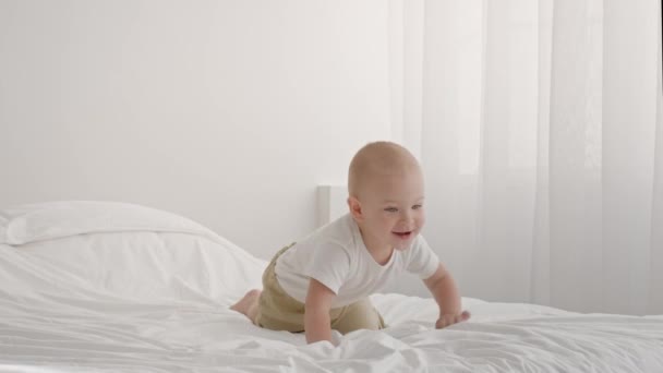 Suloinen pikkulapsi ryömii ja kiipeää sängystä kotona - Materiaali, video