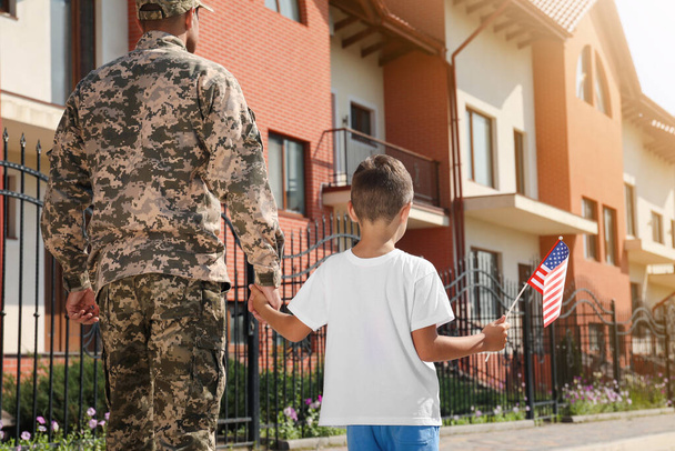 Soldier and his little son with American flag outdoors, back view. Veterans Day in USA - Photo, image