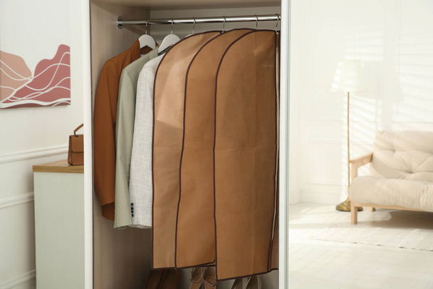Garment bags with clothes on rack in wardrobe indoors - Fotoğraf, Görsel