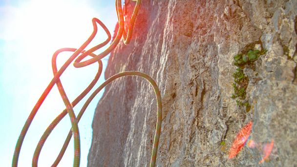 CLOSE UP, LENS FLARE: La cuerda verde y roja cae desde la cima de un imponente acantilado. - Foto, imagen