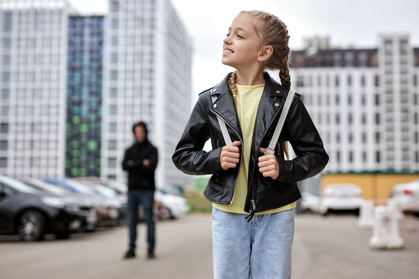 Portrait of happy smiling child girl walking alone on street, while terrible maniac looking at her - Foto, imagen
