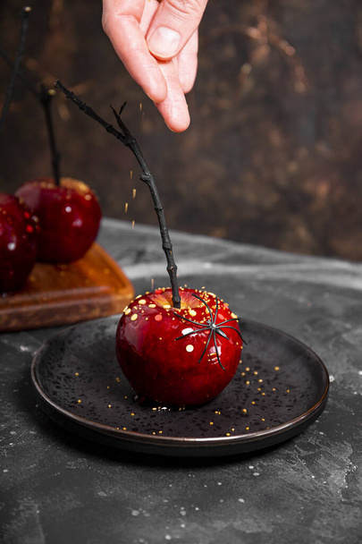 Spruzzando una mela rossa in caramello con decorazioni di zucchero, un regalo originale per un tavolo festivo di Halloween - Foto, immagini