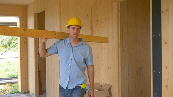 CERRAR: Feliz carpintero llevando una larga tabla mira alrededor de la casa CLT. - Foto, Imagen