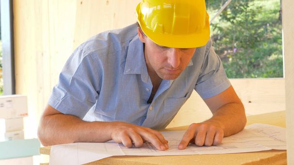 FECHAR UP: Carpinteiro olha para plantas e observa a casa em construção. - Foto, Imagem