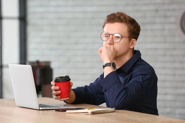 Thoughtful young man with cup of coffee in office - Fotografie, Obrázek