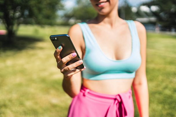 Tyttö käyttää puhelinta ja tekstiviestejä kesällä ulkona puistossa. Nainen etsii tekstiviestejä älypuhelimella. Sopiva henkilö, jolla on kännykkä ulkona bikineissä. Trendikäs elämäntapa ja mobiiliteknologia. - Valokuva, kuva