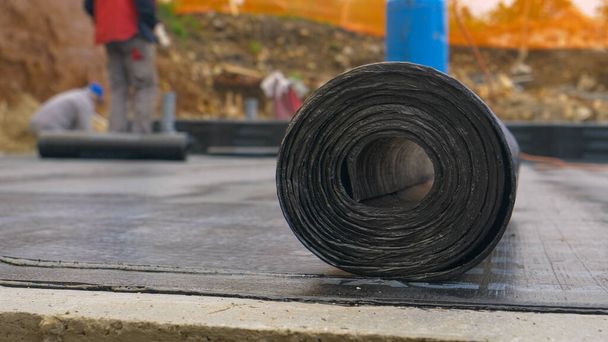 MACRO: Roll of tar lies on the ground as contractors work in the background. - Photo, Image