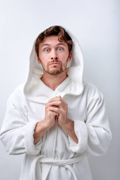 Young handsome Caucasian man wearing bathrobe against white wall praying with hands - Φωτογραφία, εικόνα