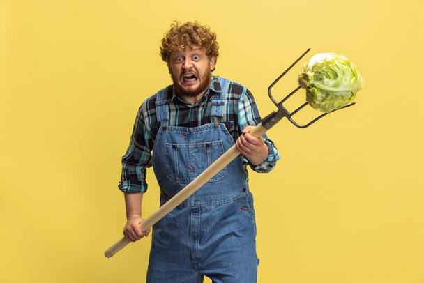 Portrait of young man, farmer with garden equipment isolated over yellow studio background. Concept of professional occupation, work. - Fotoğraf, Görsel