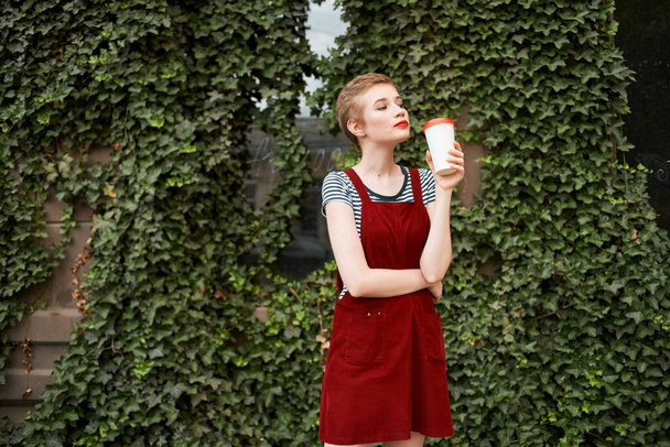 nainen, jolla on kuppi kahvia käsissään kadulla lähellä pensaita kesäloma - Valokuva, kuva