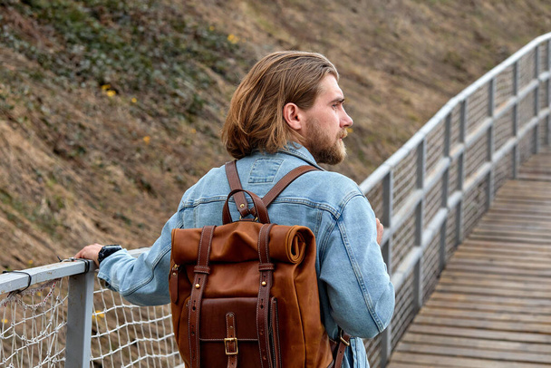 Rear view on thoughtful hipster male walking on bridge in countryside alone - Photo, Image