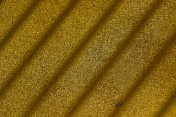 Shadow of bars of metal fence on yellow plastered wall. Diagonal lines of shadow over plaster texture. - Fotoğraf, Görsel