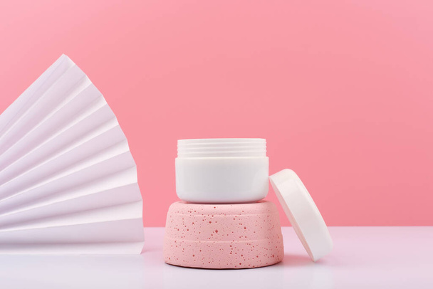 White opened cosmetic jar on pink gypsum podium against pink background with white waver and copy space. Concept of beauty product for face or hair. Face or hair cream, mask, scrub or balm - Фото, зображення