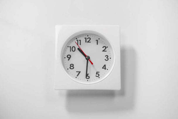Mały biały zegar ścienny pokazuje czas. Nowoczesny zegar ścienny. Blisko do zegara ściennego, ze wskaźnikiem czasu pracy i czerwonym drugim wskaźnikiem. Cień porusza się w świetle dnia..  - Zdjęcie, obraz