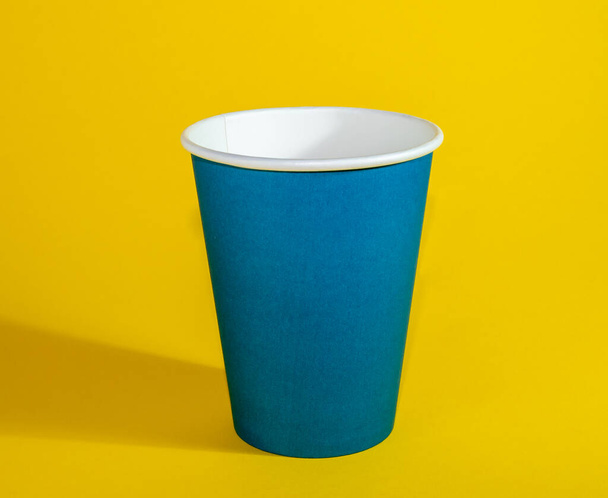 Copa de papel azul, taza desechable sobre fondo amarillo. - Foto, Imagen