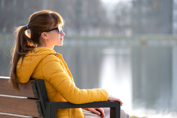 Nuori nainen istuu puistossa penkillä rentoutuen lämpimänä kevätpäivänä. - Valokuva, kuva