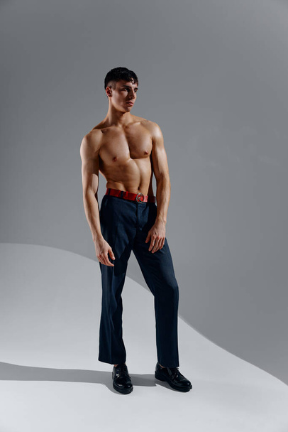 guy athlete with a pumped-up torso bodybuilder Fitness gray background jeans shoes  - Fotó, kép