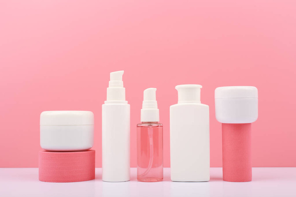 Trendy composition in pink colors with set of cosmetic bottles with beauty products on geometric props against pink background. Concept of organic cosmetics for anti acne or anti aging treatment - Foto, Bild