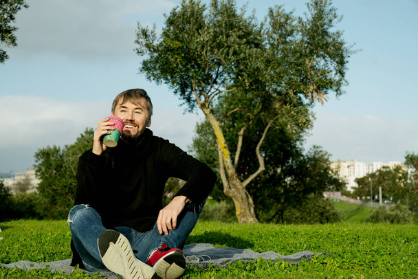 Одинокий, одинокий мужчина средних лет, пьющий кофе в парке. Концепция одиночества, социального дистанцирования и самовоспитания. Концепция психического здоровья, связанная с природой - Фото, изображение
