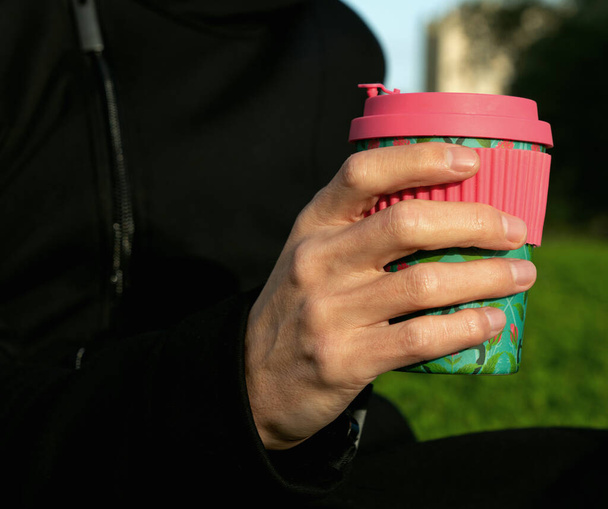 Mano masculina sosteniendo una taza de café de bambú. Beber café en el parque. Concepto de sostenibilidad. Bebidas para llevar - Foto, Imagen