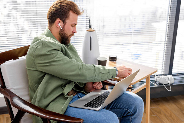 Handsome man tech user using laptop computer, wearing headphones, side view - 写真・画像