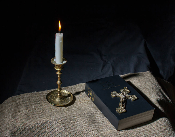 cruz de bronce, vela encendida y biblia en la mesa - Foto, Imagen