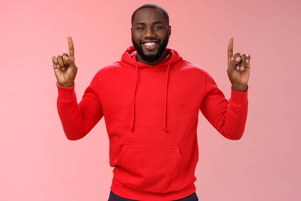 Дивовижний милий афро-американський бородатий хлопець у червоному светрі, усміхнений таємничий знає точно, що ви хочете, вказуючи підняті індексні пальці вгору посміхаючись показати ідеальний простір копіювання промо, рожевий фон
 - Фото, зображення